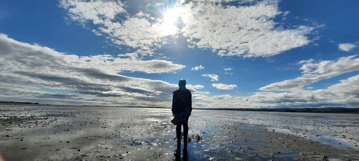 A person looking into a vast land mass revealed by a low tide.