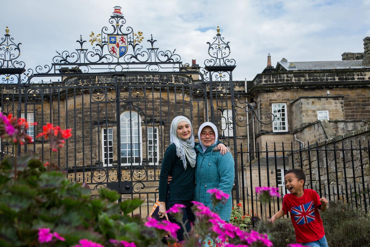 Two smiling women posing to a camera while a joyful child runs around them.