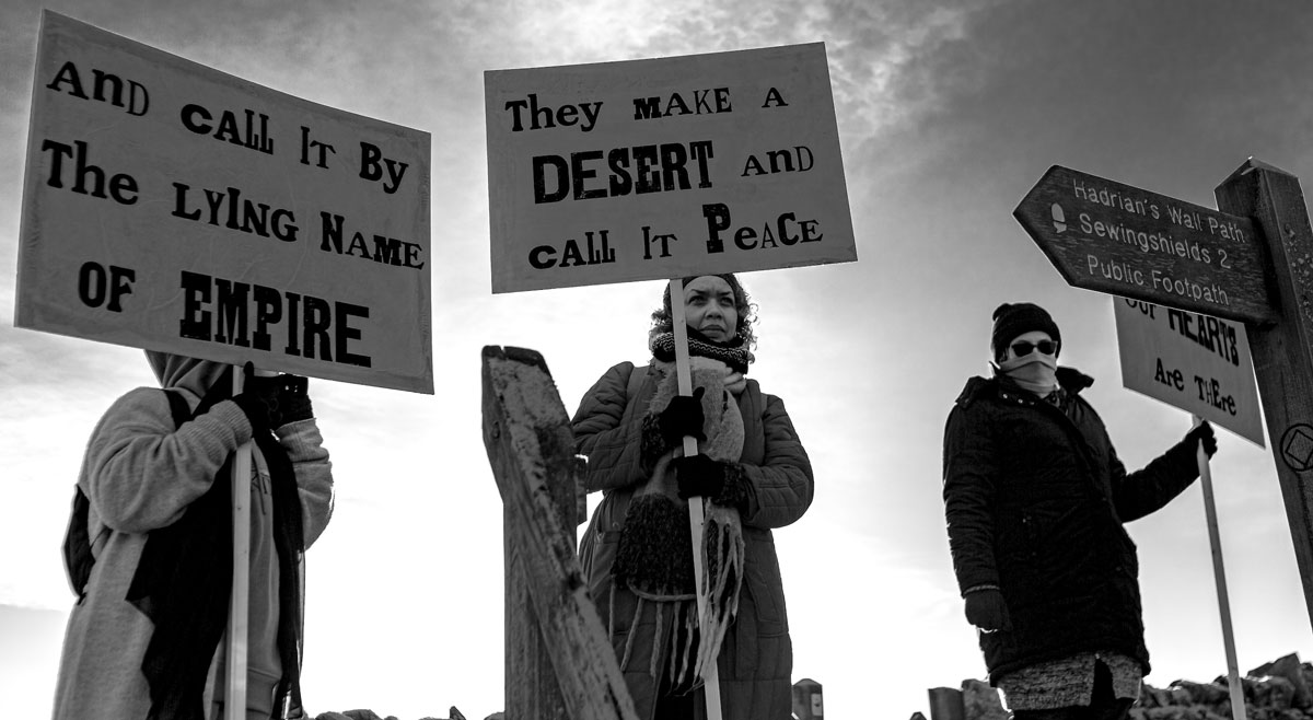 Three people holding banners by Hadrian’s wall.