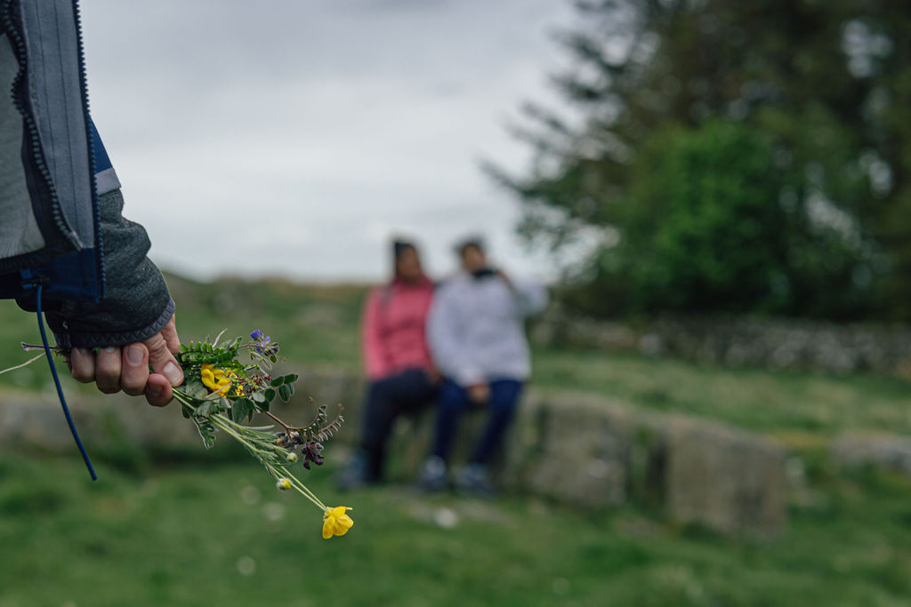 A hand holding flowers, two people sit in the background.