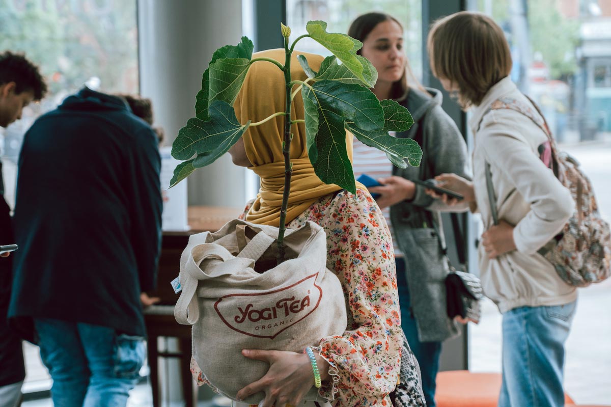 A woman carrying a young tree in a cloth bag.